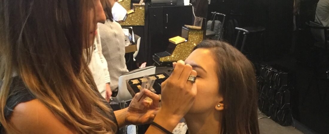 Maquilladora aplicando sombra de ojos a una asistente en el estand de una feria de belleza