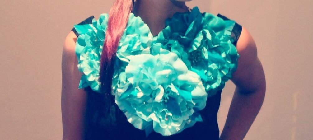 Joven con coleta y mechón rosa llevando un vestido negro con grandes flores de tela turquesa