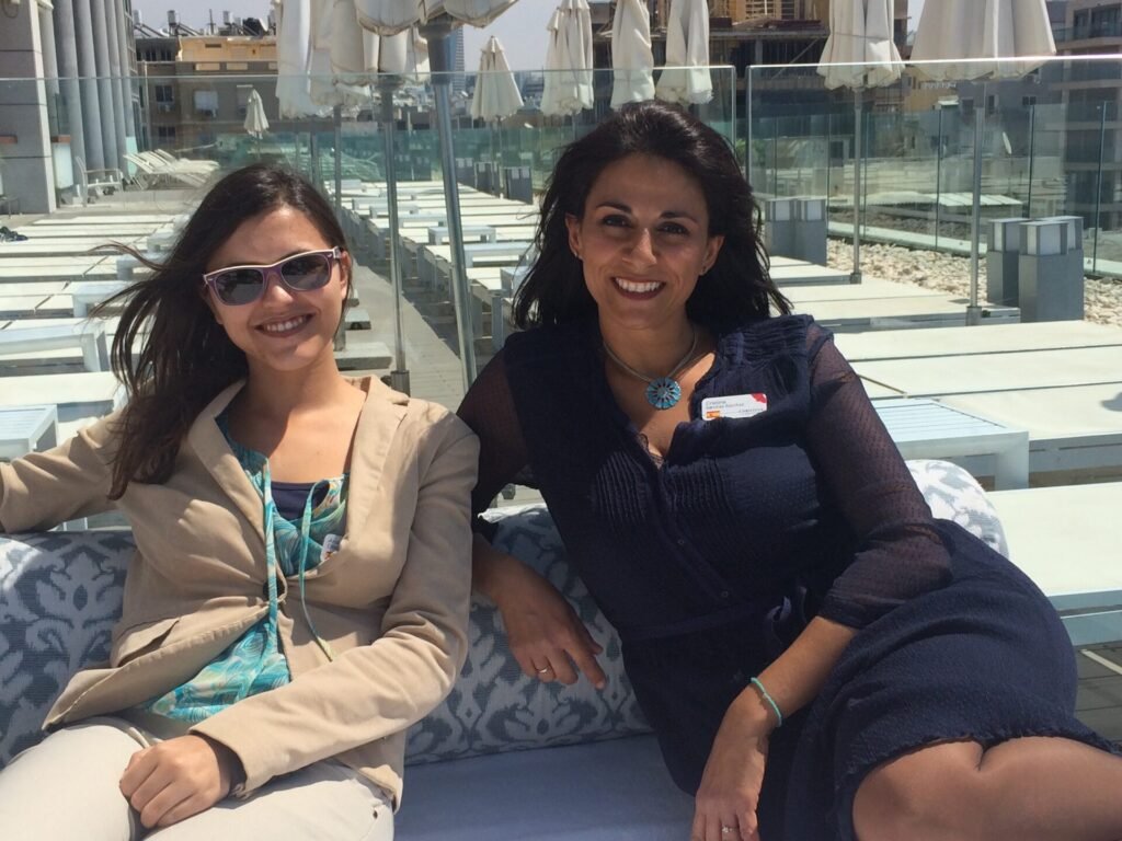 Dos mujeres sonrientes sentadas en un sofá de terraza, con hamacas y sombrillas cerradas al fondo