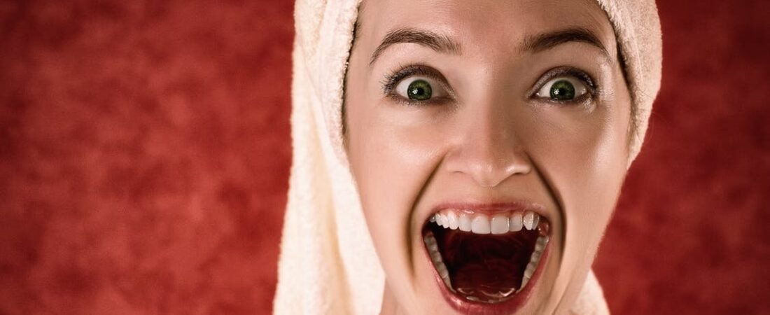 Mujer con turbante de toalla y la boca muy abierta en gesto de sorpresa sobre fondo rojo