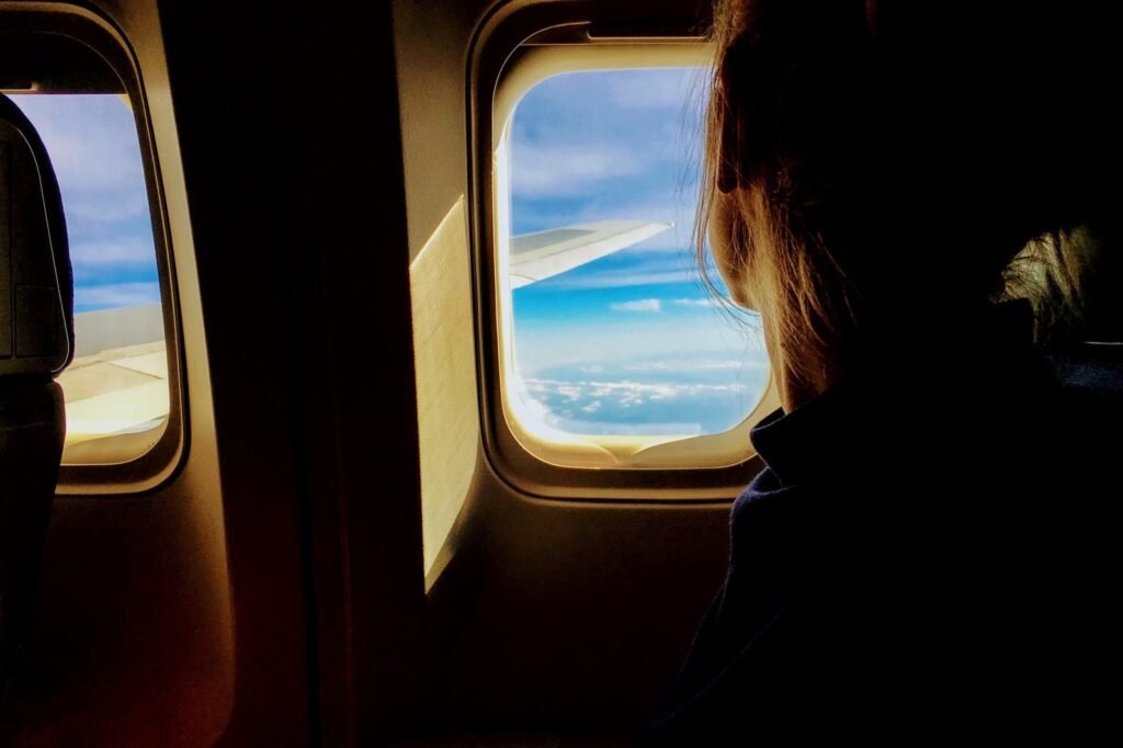 Pasajera de espaldas mirando por la ventanilla de un avión con el ala y las nubes al fondo