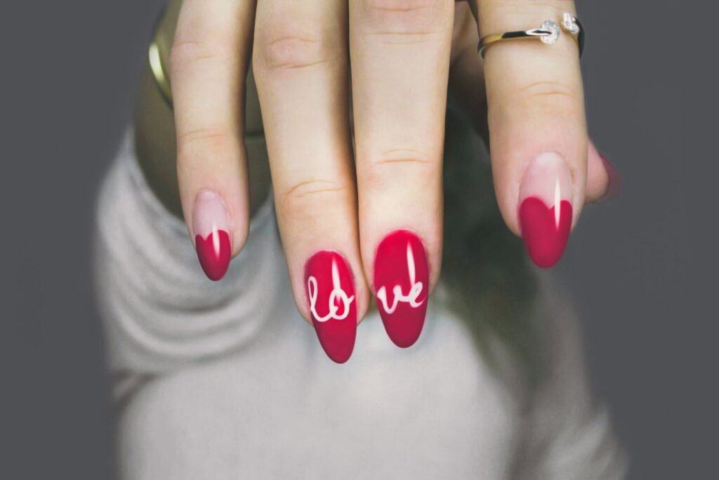 Mano con uñas almendradas rojas decoradas con corazones y la palabra Love