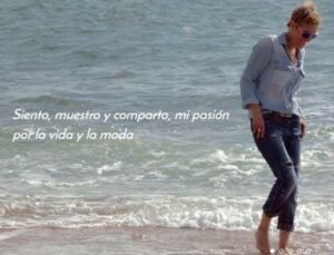 Mujer con camisa vaquera caminando por la orilla del mar junto a la frase Siento, muestro y comparto mi pasión por la vida y la moda
