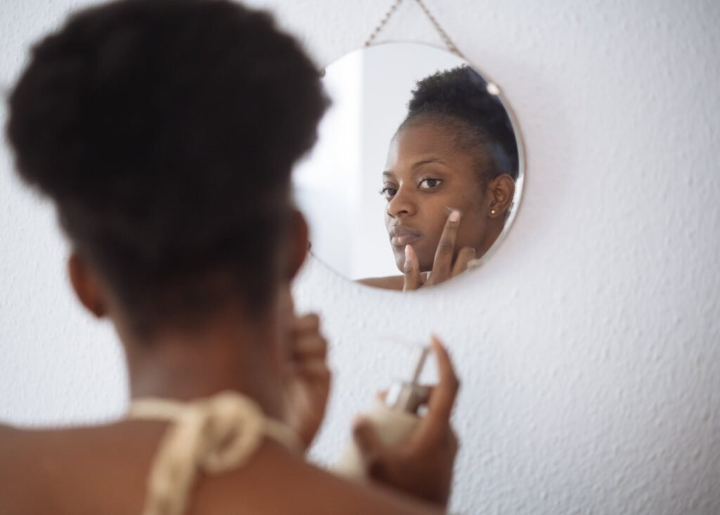 Mujer aplicándose crema en la mejilla reflejada en un espejo redondo colgado de la pared