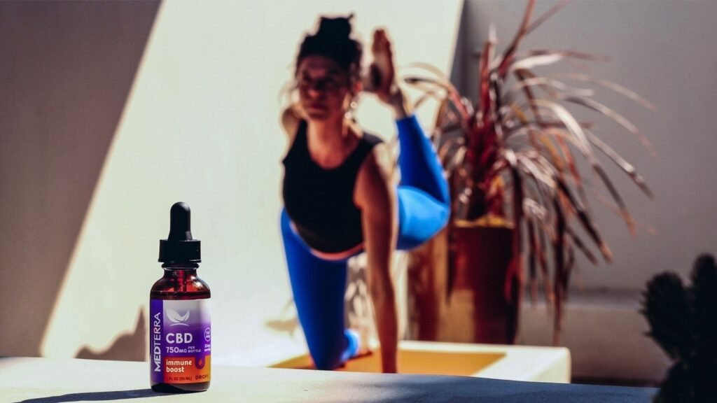 Frasco de aceite de CBD Medterra en primer plano con una mujer haciendo yoga desenfocada al fondo