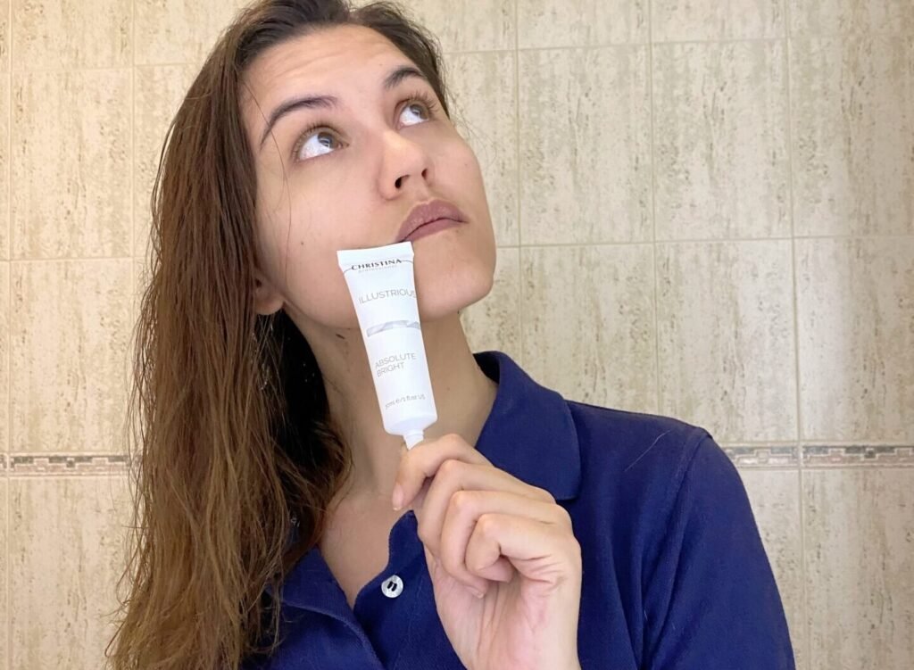 Mujer con polo azul sosteniendo un tubo de crema despigmentante Illustrious Absolute Bright