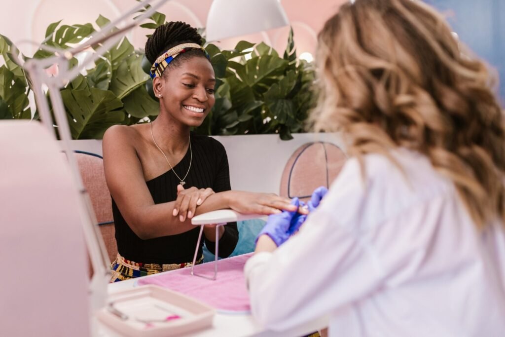 Clienta sonriente recibiendo una manicura de una profesional con guantes en un salón rosa con plantas