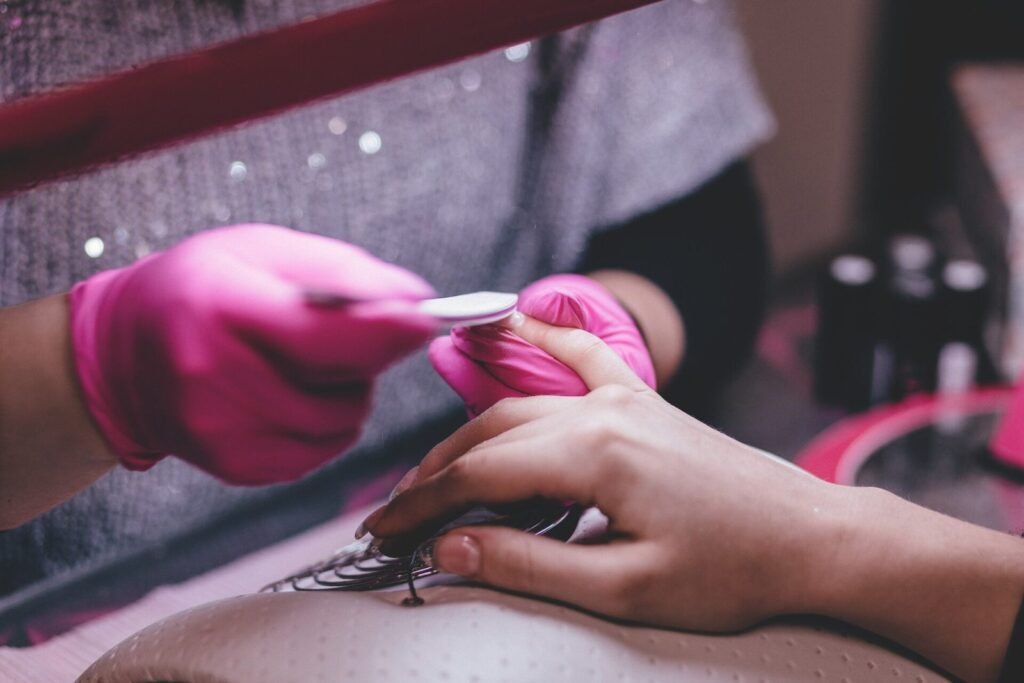 Manicurista con guantes rosas limando las uñas de una clienta en el salón