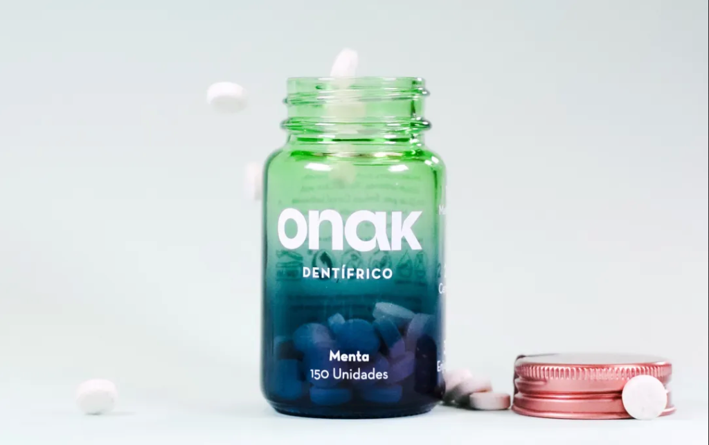 Bote de vidrio verde y azul de pastillas de dentífrico Onak sabor menta, con la tapa rosa al lado
