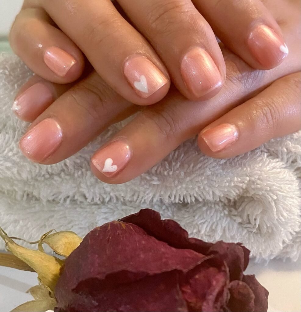 Manos con manicura rosa nacarada y corazones blancos sobre una toalla, junto a una rosa seca