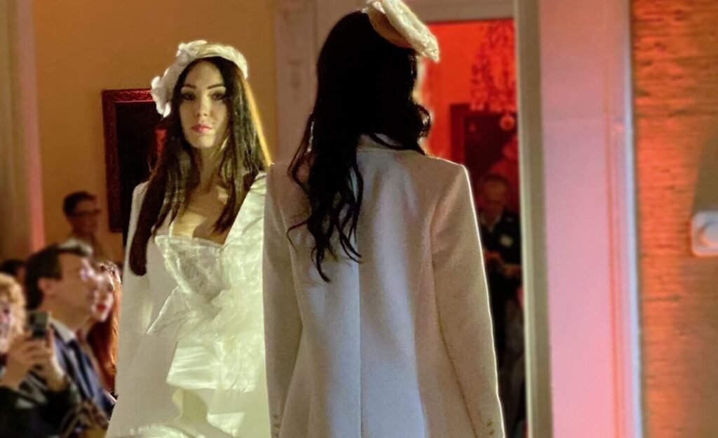 Dos modelos con vestido y abrigo blancos de novia desfilando ante el público