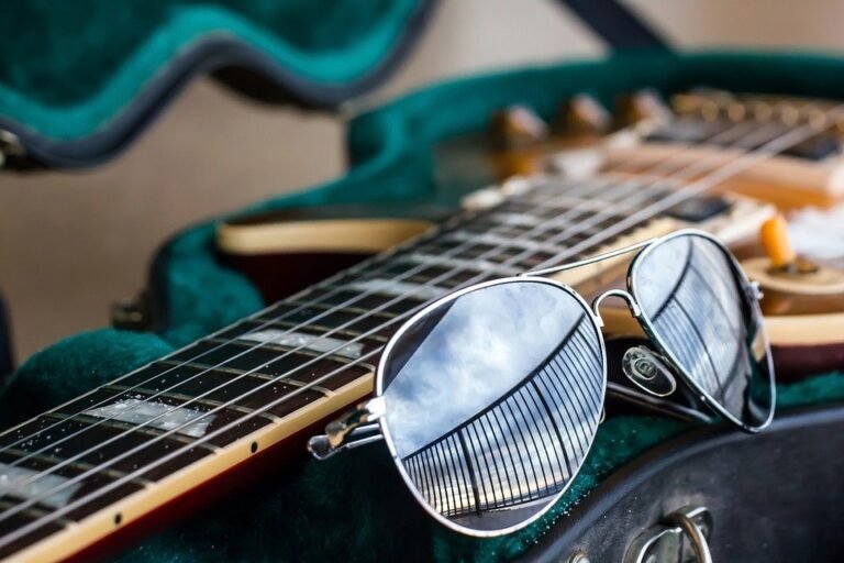 Gafas de aviador espejadas apoyadas en el mástil de una guitarra eléctrica dentro de su funda verde