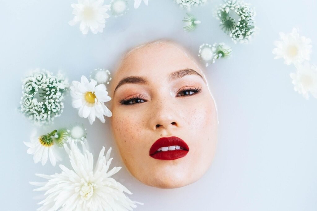 Rostro de una mujer con labios rojos en un baño de leche rodeado de flores blancas