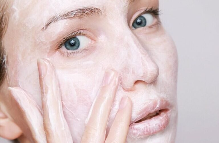 Primer plano de una mujer aplicándose una mascarilla cremosa en la cara con los dedos